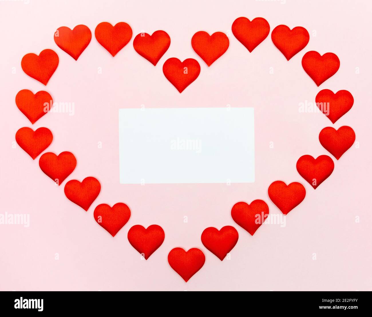 Big heart of small hearts with a sheet of paper inside mock-up on a pink background. Concept of holidays and Valentines Day. Stock Photo
