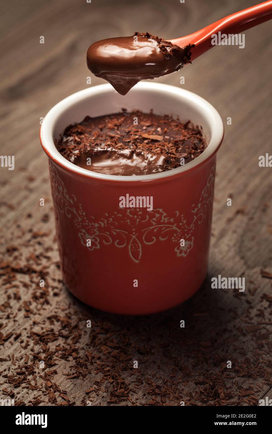 chocolate pudding in a red pot with cream on a spoon and chocolate chips on the grey table Stock Photo