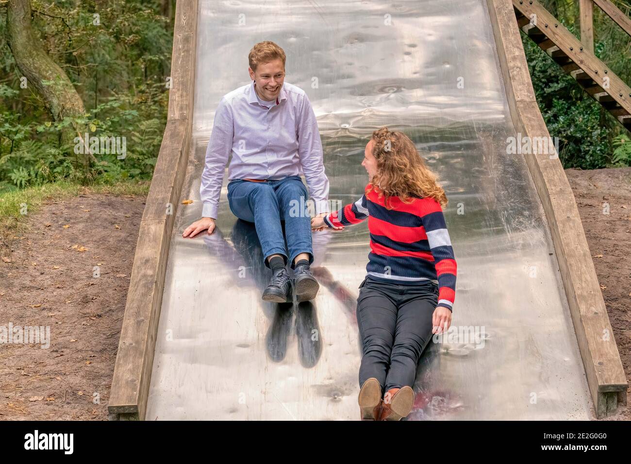 Young couple having a lot of fun on a big metal slide in the woods. they  look at each other Stock Photo - Alamy