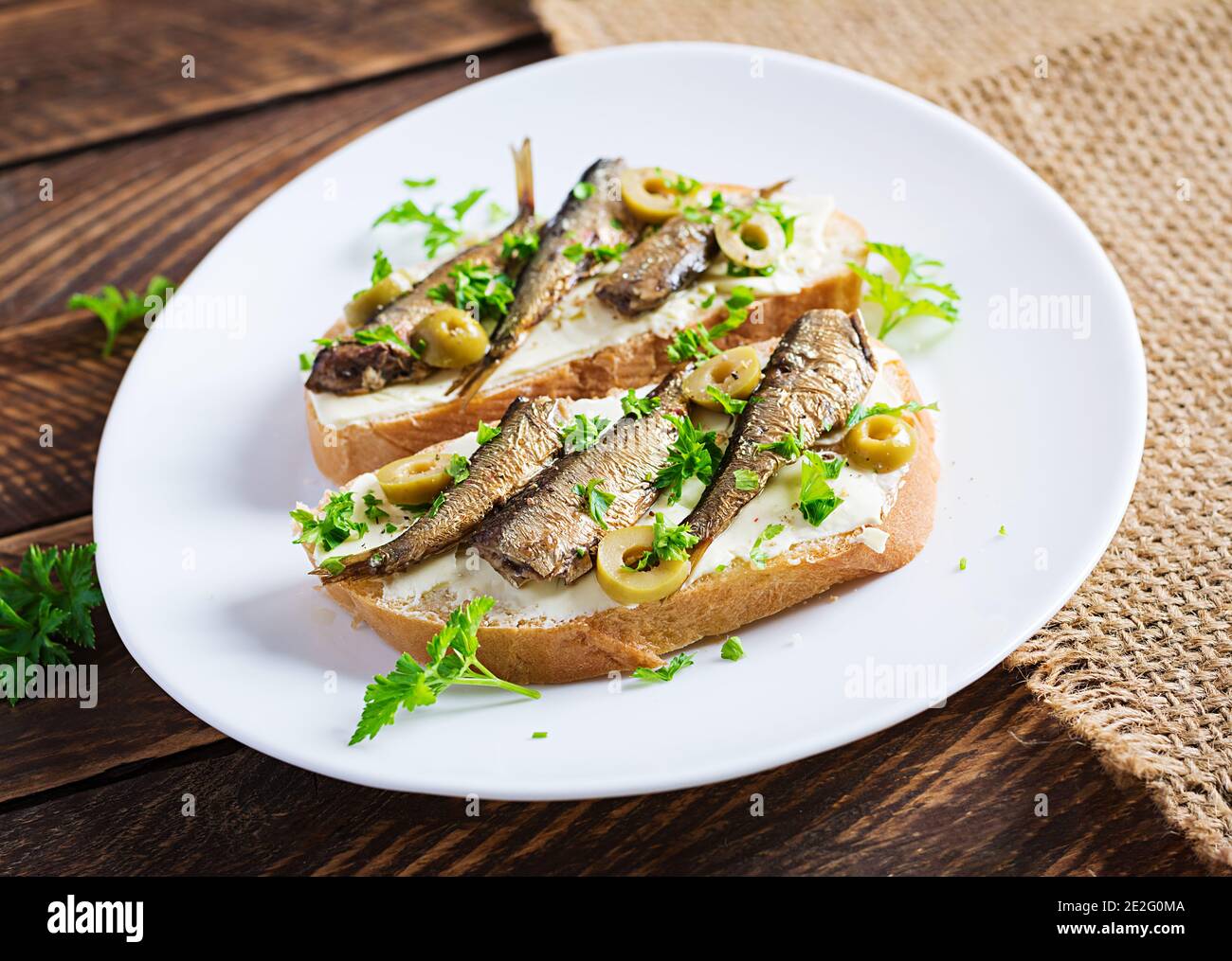 Sandwich - smorrebrod with sprats, green olives and butter on wooden table. Danish cuisine. Stock Photo