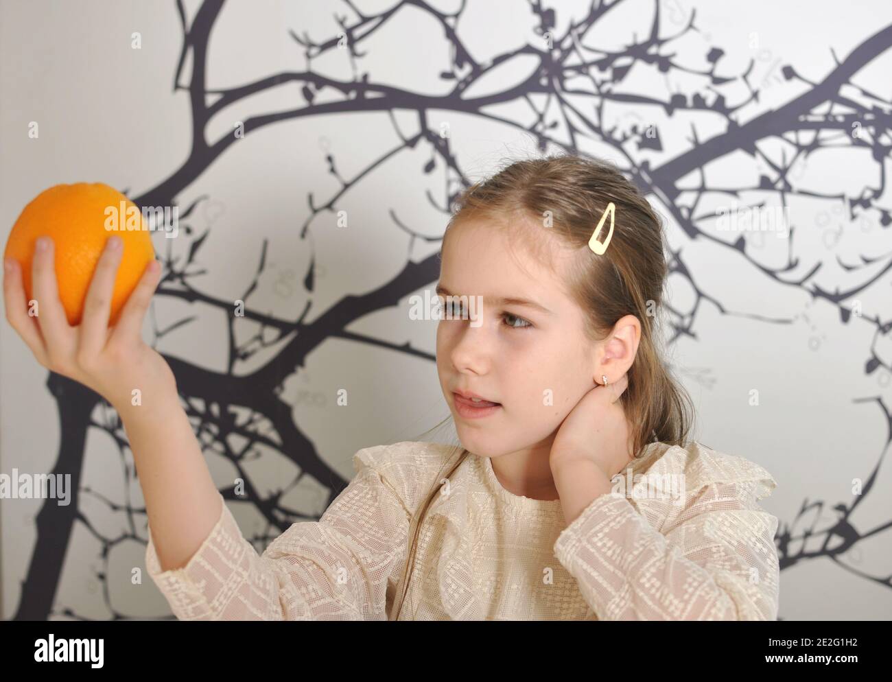 White girl (child, kid) smiling and looking at an orange hold in her hand. Stock Photo
