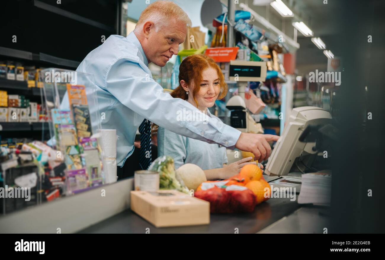 Senior manager training a new female employee at checkout counter. New cashier getting some help from store manager. Stock Photo