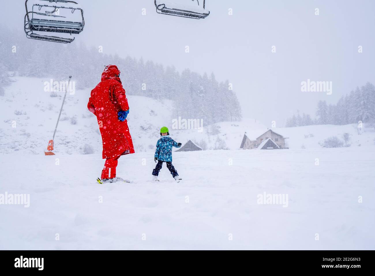 Professional ski instructor is teaching a child to ski on a mountain slope. Snowfall day. Family and children active vacation concept. Blurred focus background.  Stock Photo