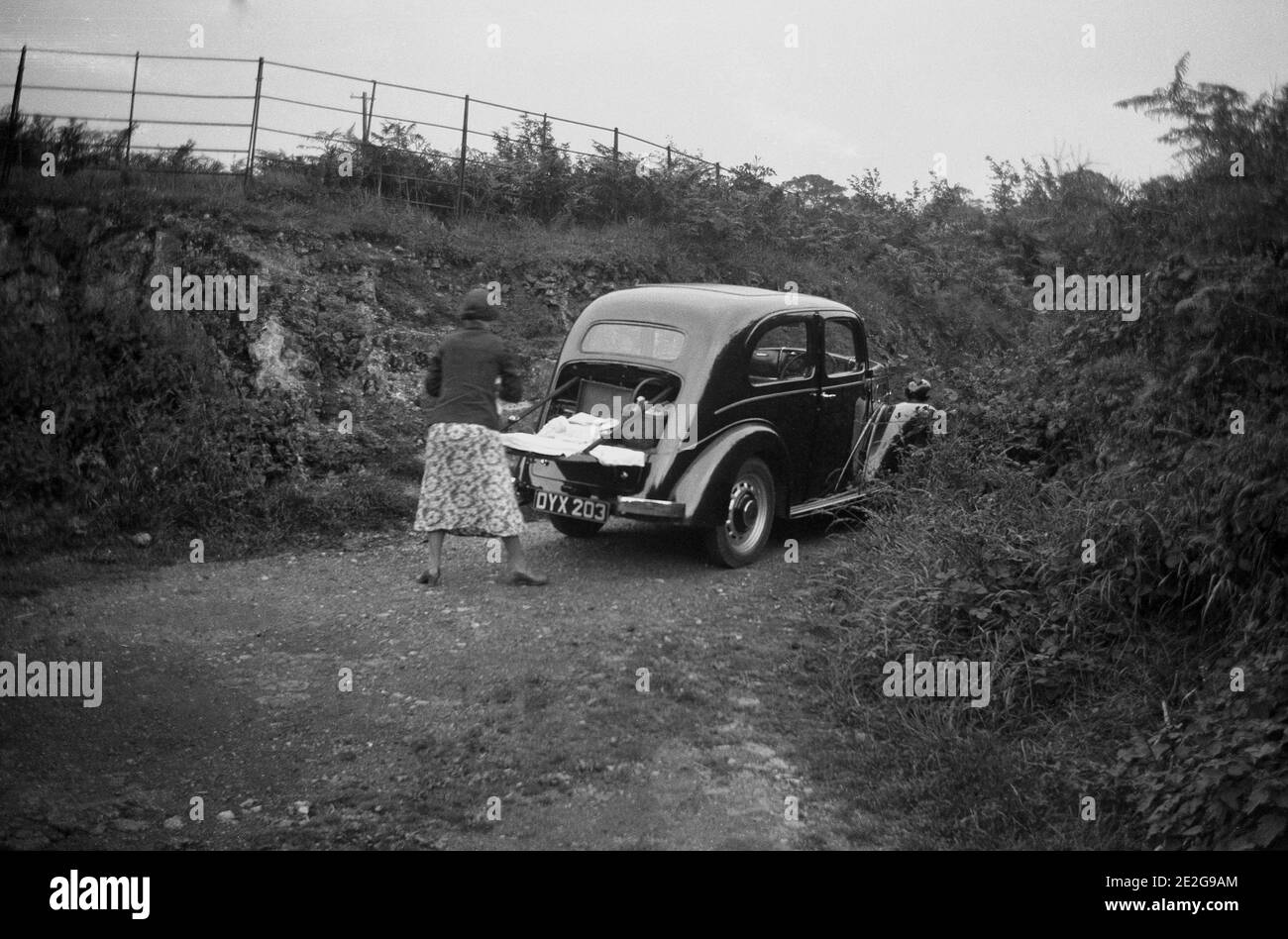 1940s, historical, a lady with her car of the era with its boot open and folded down, with what looks like a picnic, having stopped in a secluded, high walled, rural lane, England UK. Stock Photo