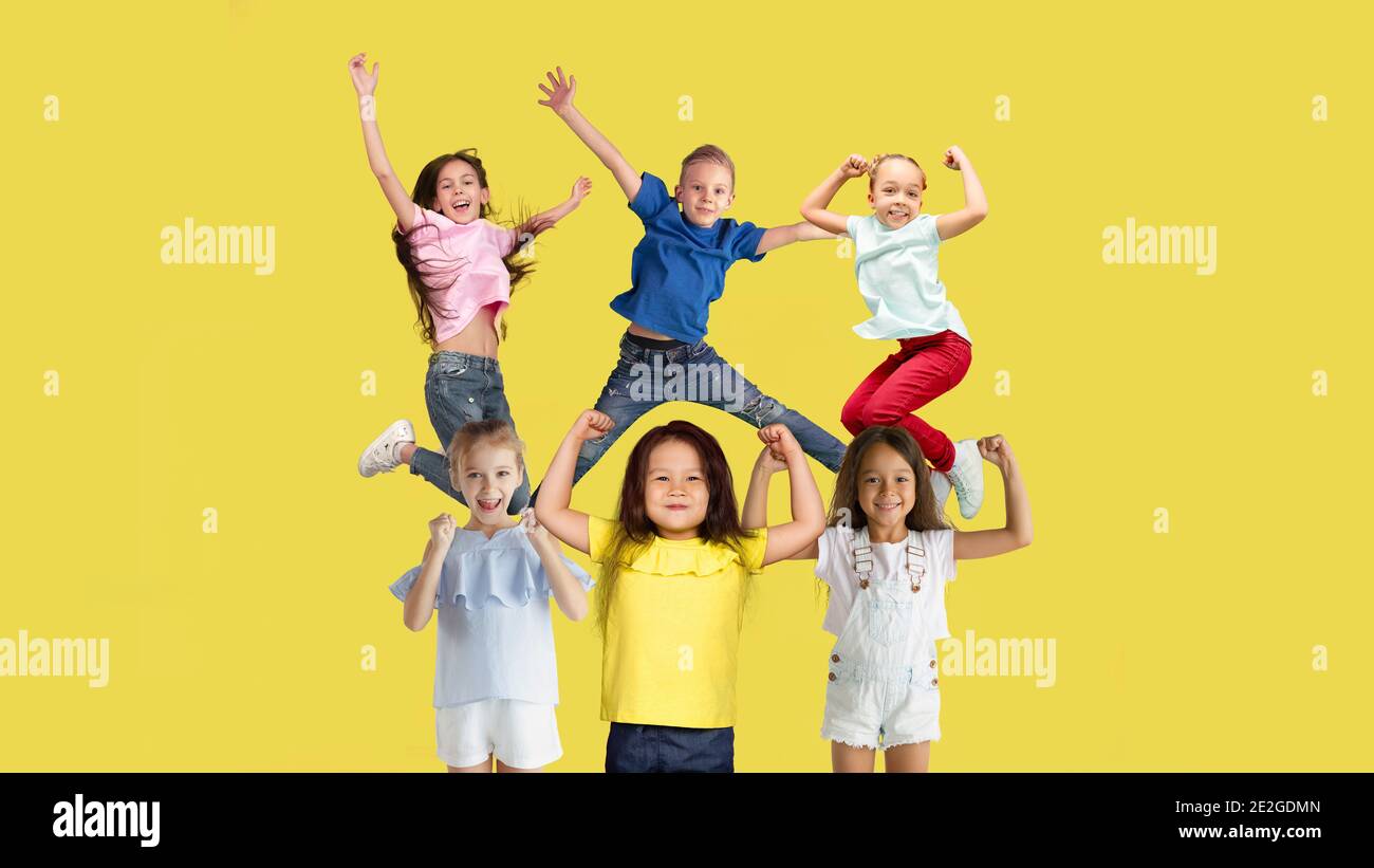 Happy. Portrait of little caucasian children jumping isolated on yellow studio background with copyspace. Cheerful kid models. Concept of human emotions, facial expression, sales, ad, childhood. Stock Photo