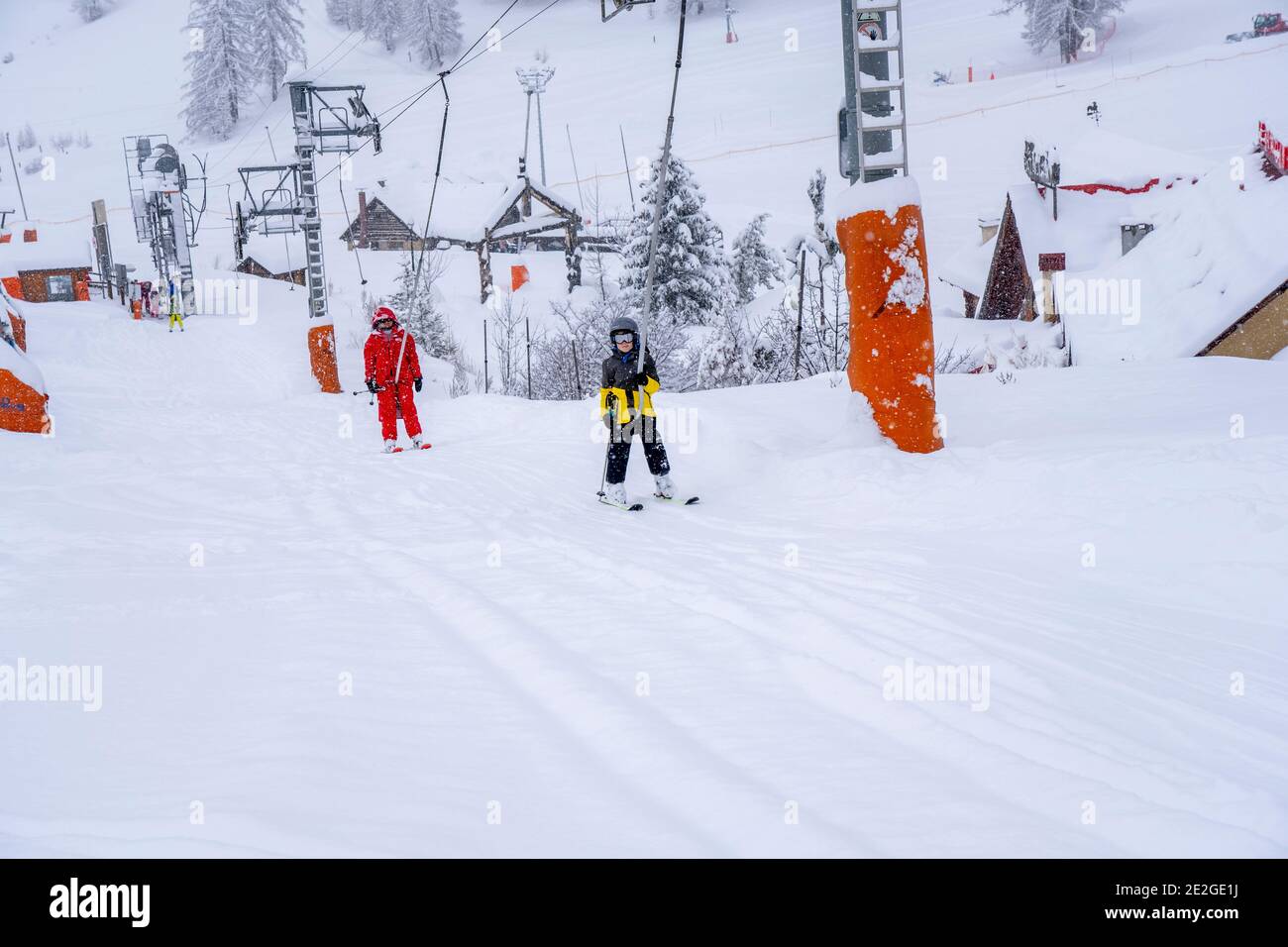 AURON, FRANCE-01.01.2021: Professional ski instructor and child lifting on the ski drag lift rope to the mountain during snowfall. Family and children Stock Photo
