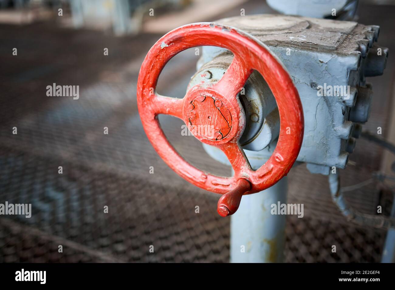 Old rusty steampunk electro valve wheel painted red paint swellings peeling selective focus with handle grip over out of focus background floor and Stock Photo