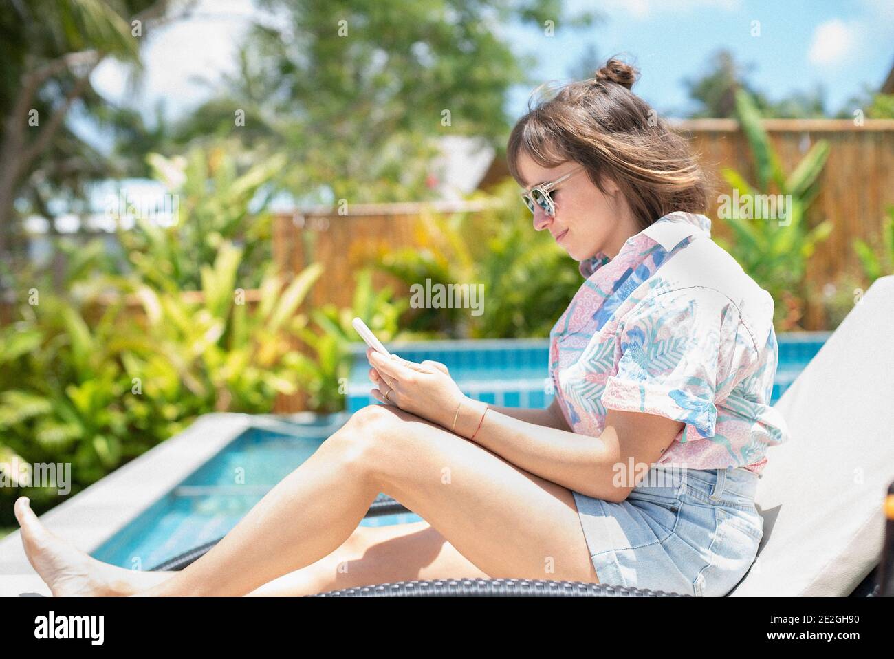 Woman using smart phone on sunny poolside lounge chair Stock Photo