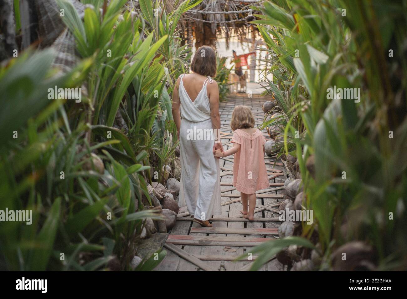 Mother and daughter holding hands on tropical resort boardwalk Stock Photo