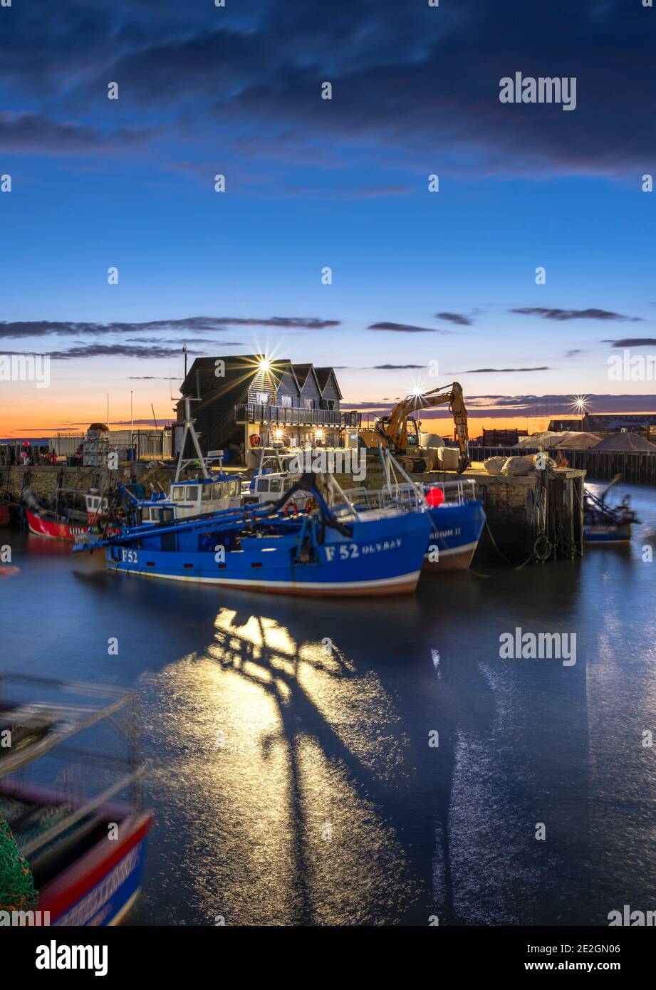 Fishing vessels in Whitstable harbour illuminated at dusk on the North Kent coast. Stock Photo