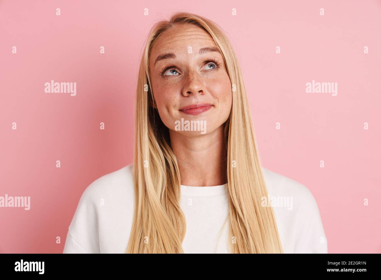 Cheerful beautiful girl smiling and looking upward isolated over pink ...