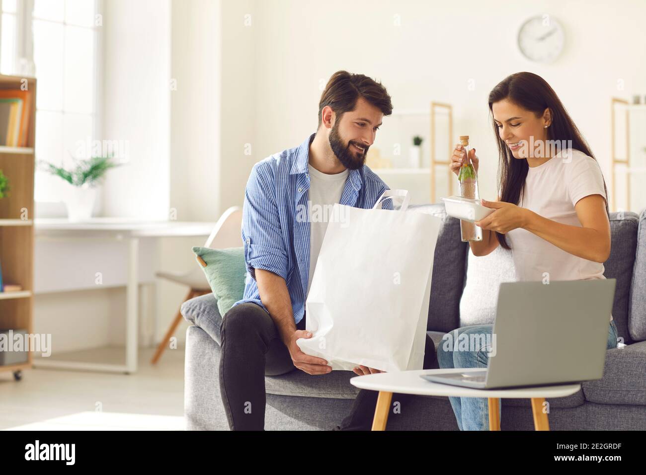 Happy young couple taking their meal delivery order out of paper bag sitting on couch at home Stock Photo