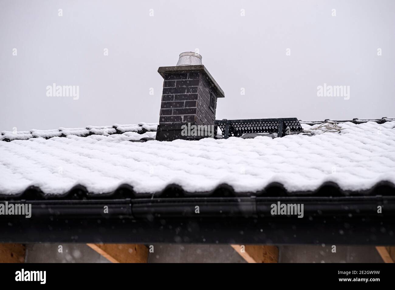 The roof of a detached house is covered with snow against a cloudy sky ...