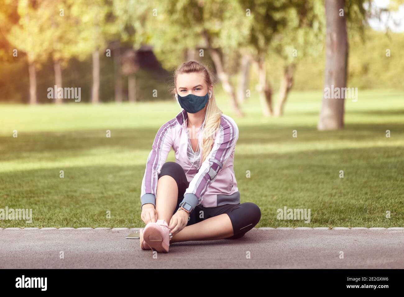 Mature woman with face mask tying sport shoes before running Stock Photo
