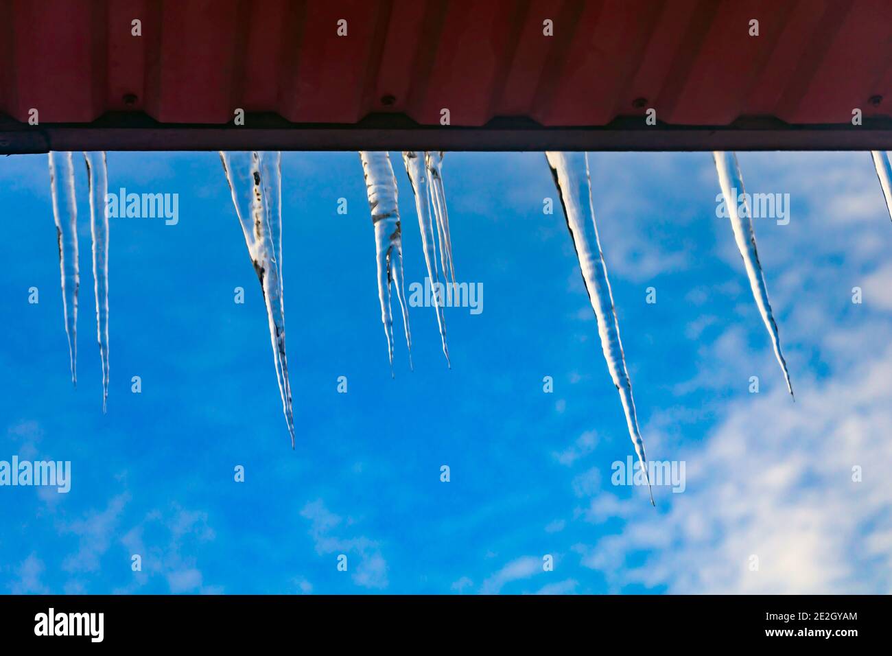 beautiful icicles shine in the sun against the blue sky. landscape with ice icicles hanging from the roof of the house Stock Photo