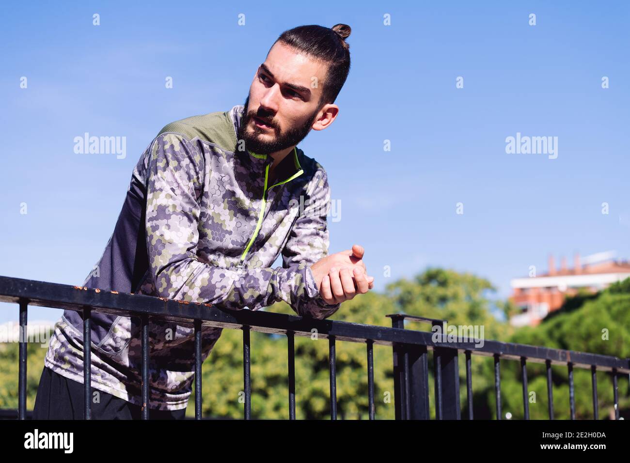 handsome sportsman with hair in a chignon resting on a railing, concept of healthy lifestyle and urban sport in the city, copy space for text Stock Photo