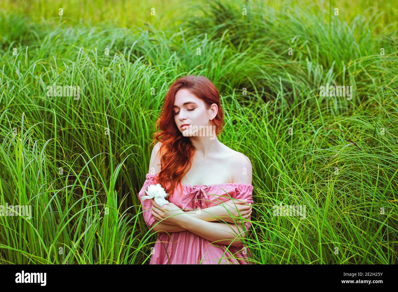 Outdoor portrait of young redhead woman in field of green grass with ...