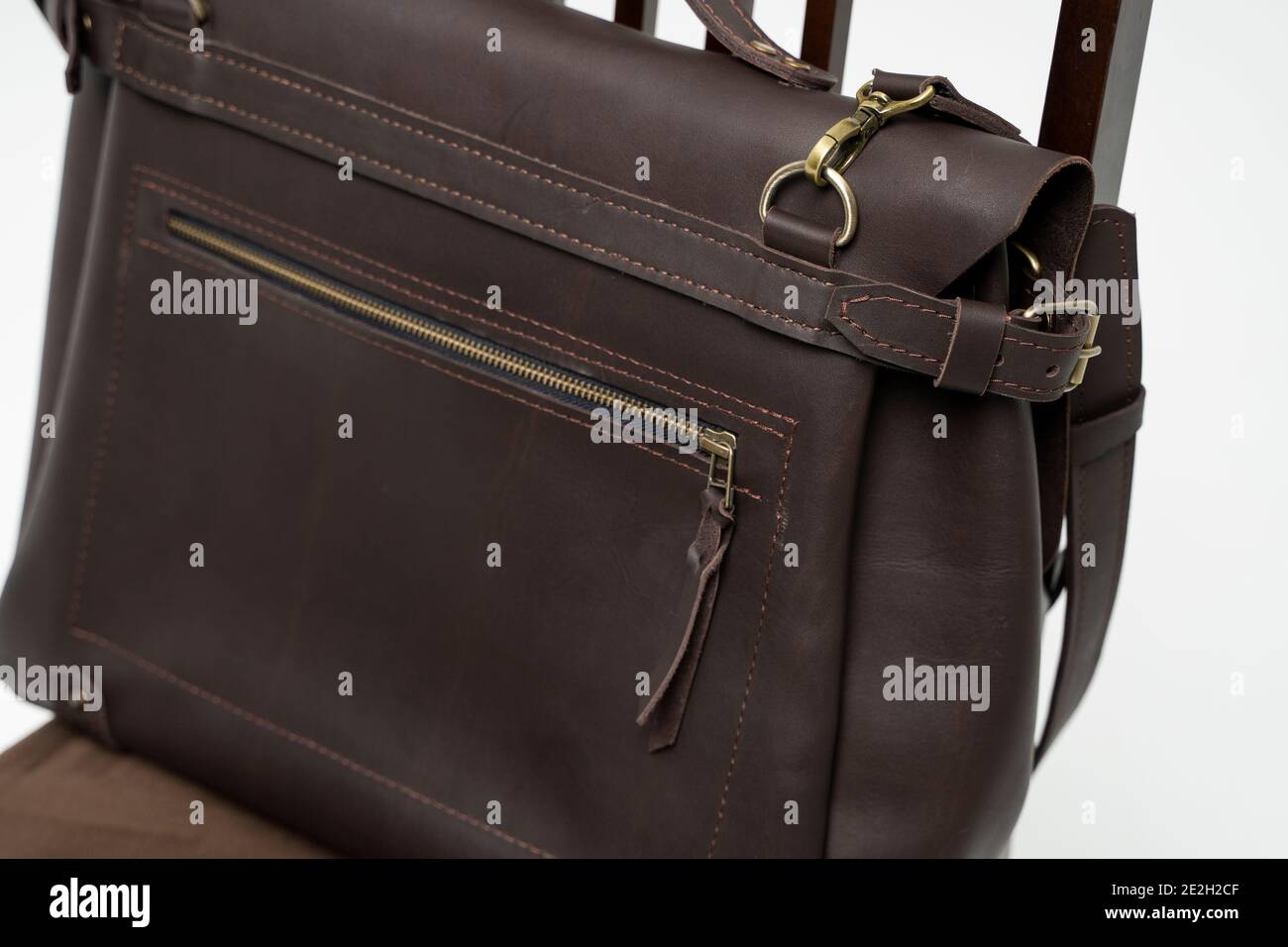 Details of brown men's shoulder leather bag for a documents and laptop on a brown chair with a white background. Mens leather brief case, messenger Stock Photo