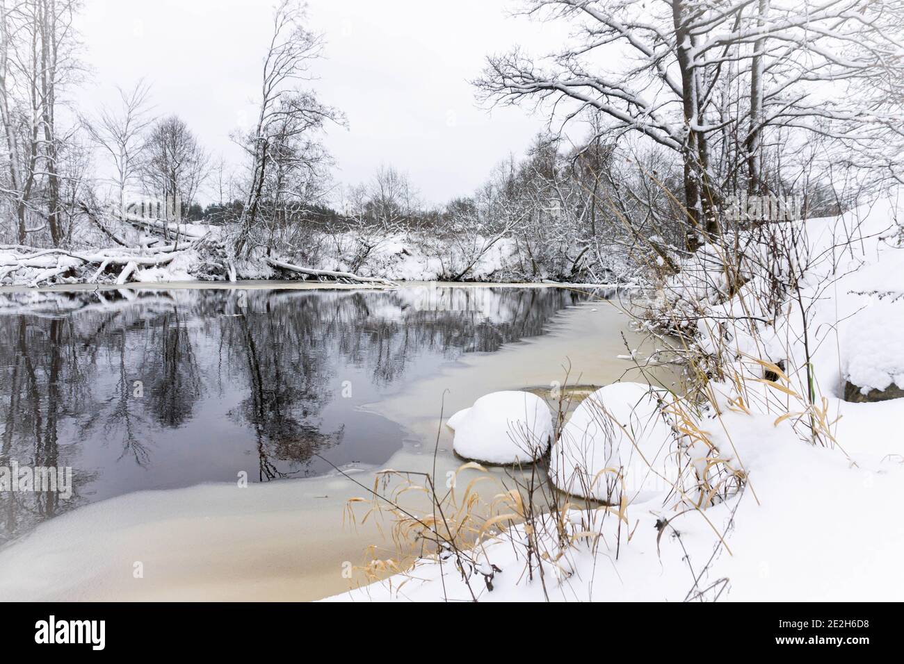 Winter scenery with snowy forest, frozen river and yellow color accents ...
