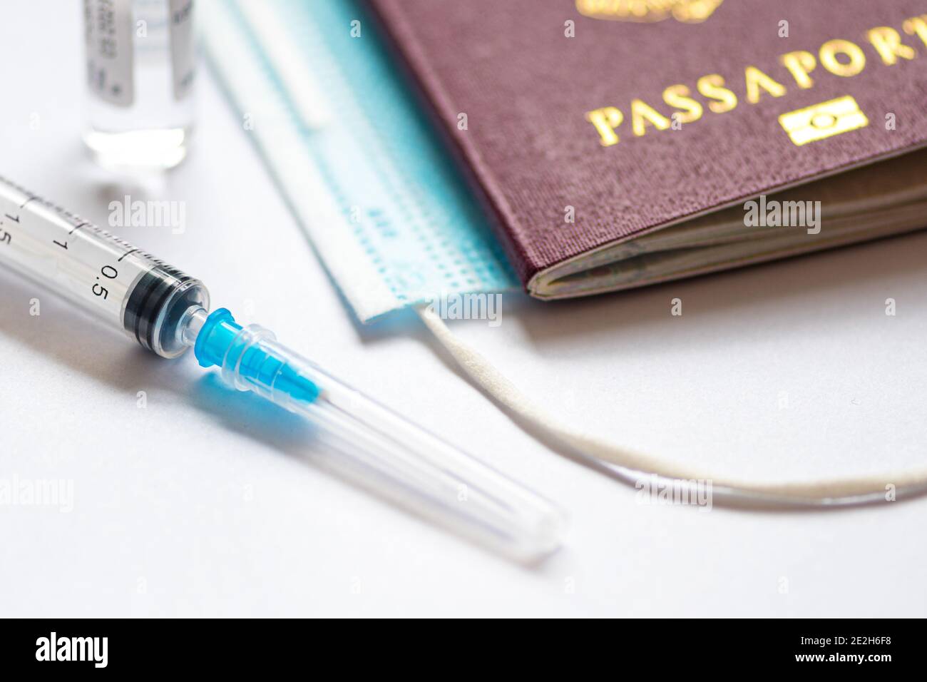 Syringe with needle, vial or phial, surgical face mask and passport or visa on a white table ready to be used. Covid or Coronavirus vaccine background Stock Photo