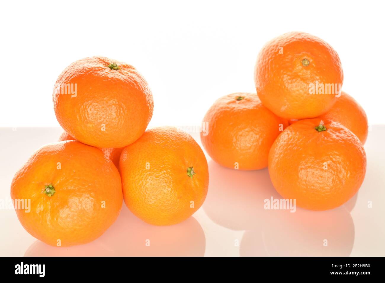A few whole bright orange ripe juicy tangerines, on a white background. The nearest mandarin, in the foreground in focus. Stock Photo