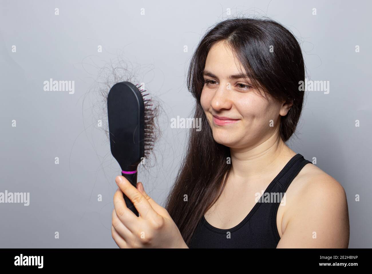The girl is holding a hairbrush with her hair falling out and smiling. Hair loss, hair care and treatment. Doctor trichologist. Stock Photo