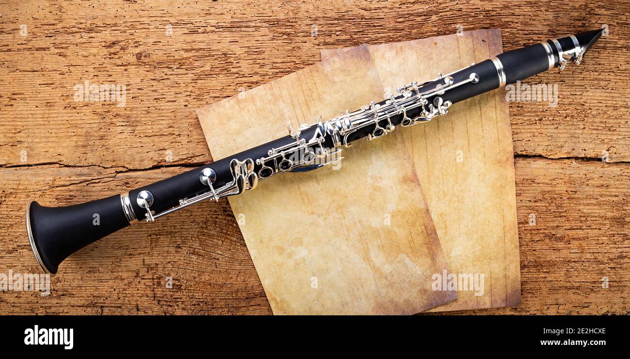 black wooden clarinet  silver woodwind musical brass instrument with old empty vintage music sheet copy space paper on retro oak wood background. clas Stock Photo