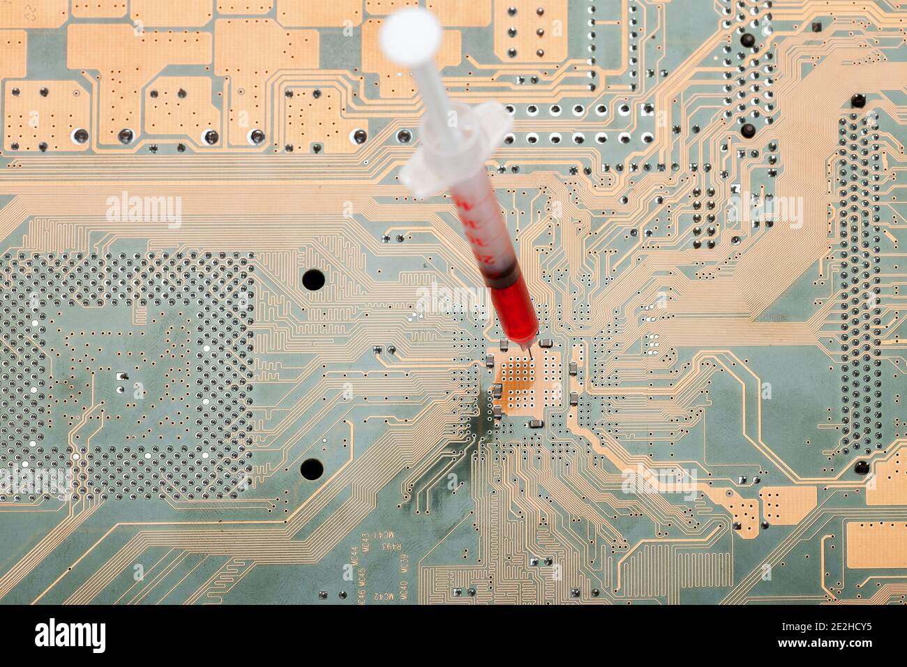 syringe with a needle filled with red vaccine against the virus vaccination circuit board intervention and chipping of humanity, conspiracy theory and Stock Photo