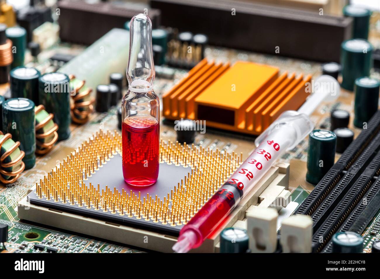 glass ampoule with red medicine with syringe on socket with cpu chip with contact legs on motherboard with microelectronic components, closeup on them Stock Photo