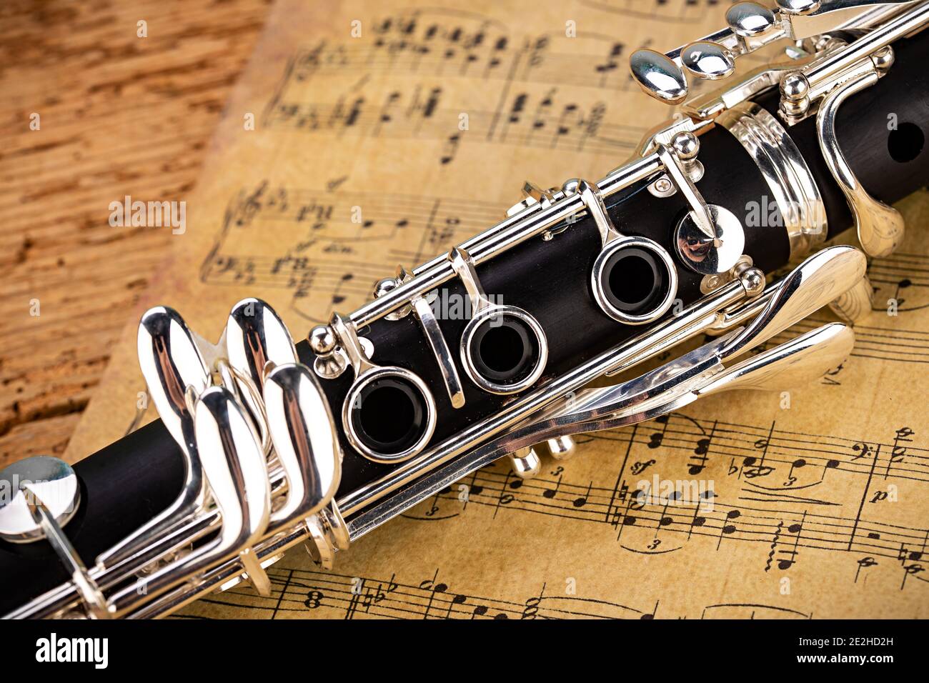 black wooden clarinet  silver woodwind musical brass instrument with old vintage music sheet paper on retro oak wood background. classic orchestra sym Stock Photo