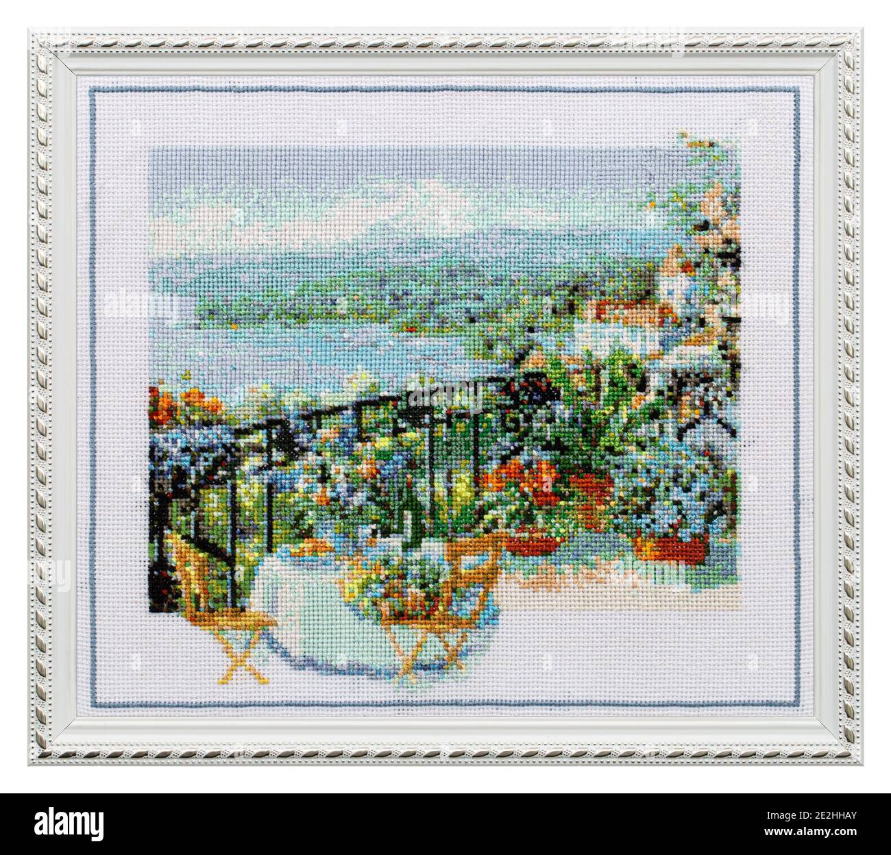 Embroidered picture in an openwork frame, outdoor cafe terrace overlooking the sea, cross-stitch on textile canvas, isolated on white background Stock Photo