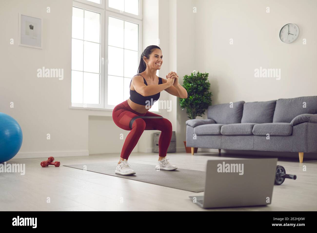 Woman working out with a rubber band in front of a laptop during an broadcast of a fitness workout. Stock Photo