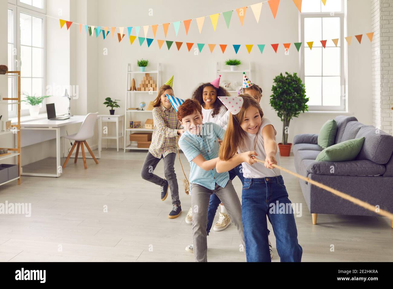 Bunch of happy multiethnic children playing tug-of-war at fun party at home or in kids club Stock Photo