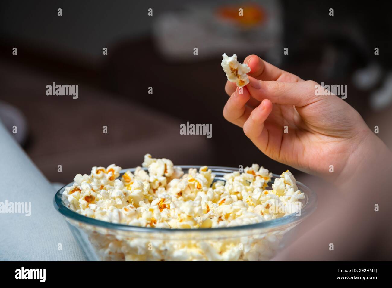 Close up of hand waking popcorn from a bowl while watching TV. Person sitting in comfortable couch and watching home cinema in the dark. Stock Photo