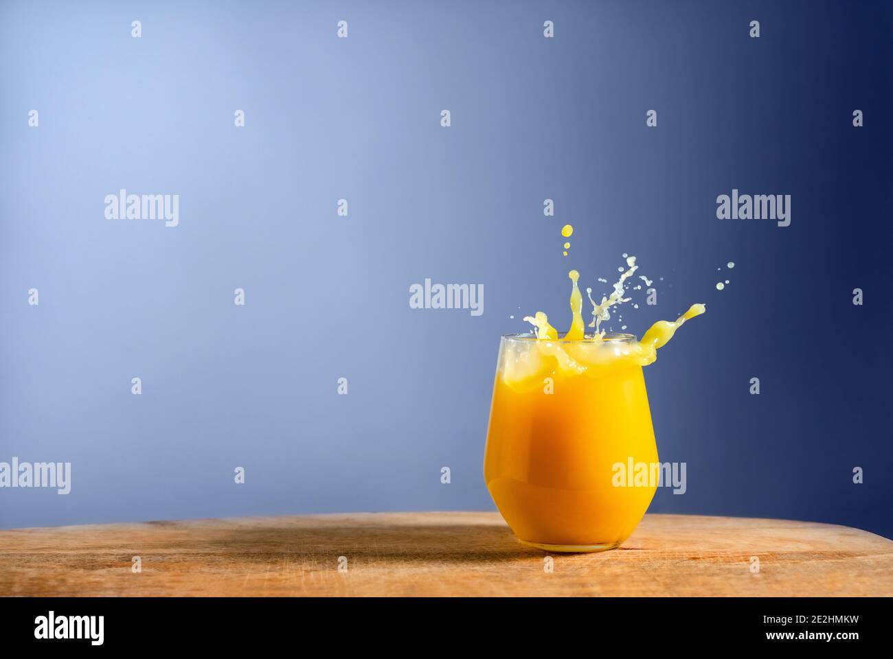 Glass of fresh orange juice splash on on wooden table and blue