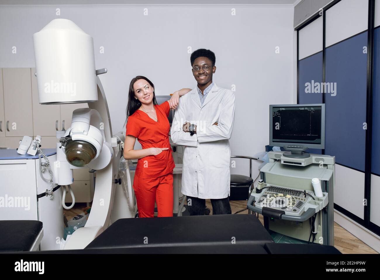 Modern medical center, non-invasive extracorporeal shock wave lithotripsy. Two happy multiethnic male and female doctors, posing to camera near modern Stock Photo