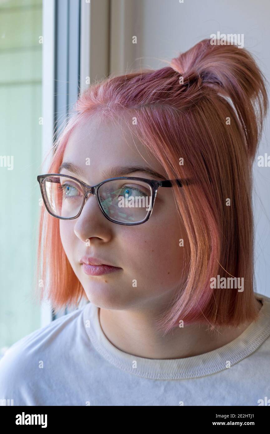 Young girl in glasses and pink hair looking aspirational whilst looking out through window Stock Photo