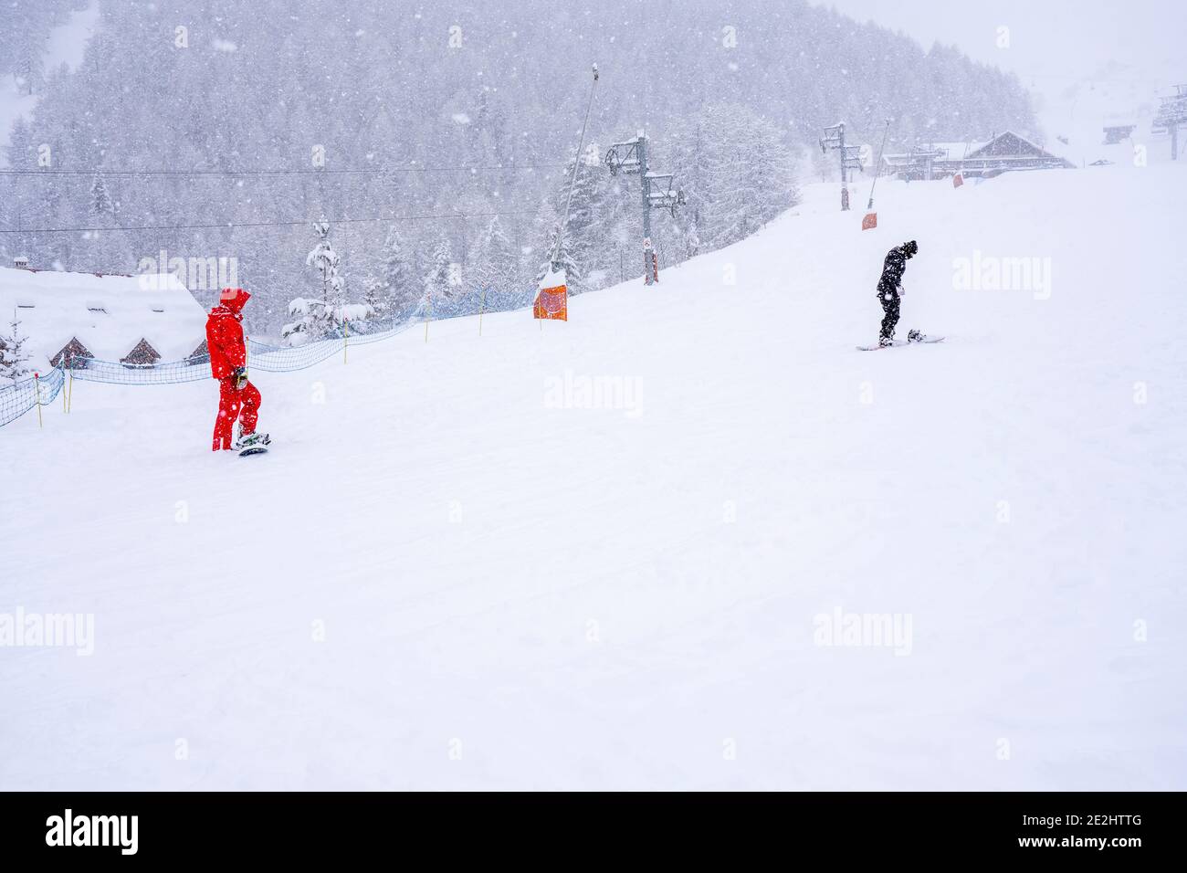 Professional instructor is teaching a boy to ride a snowboard on a mountain slope. Snowfall day. Blurred focus background. Family and children vacatio Stock Photo