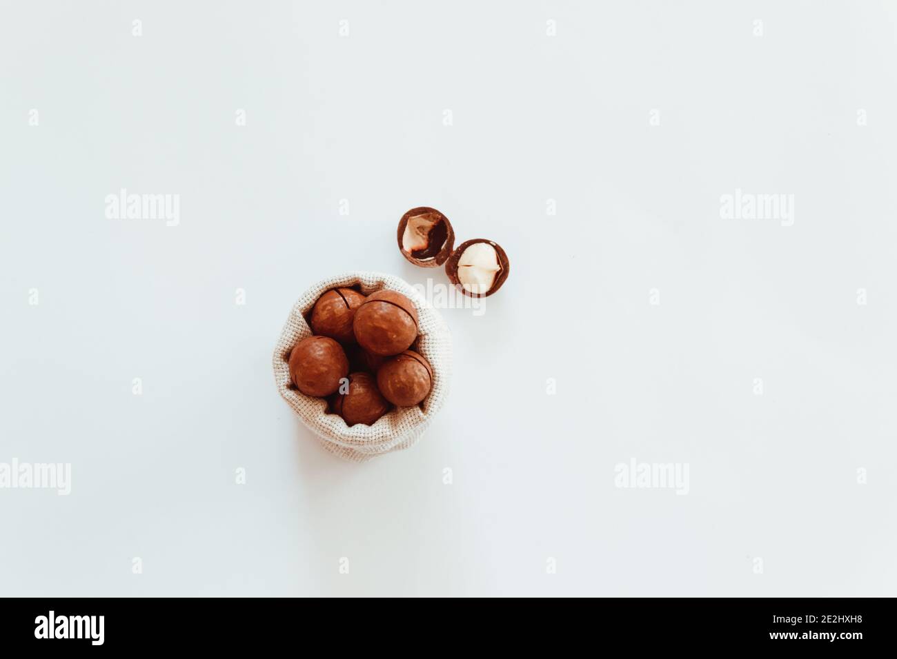 Raw macadamia nuts in canvas bowl on a white solid background. Minimal flat composition Stock Photo