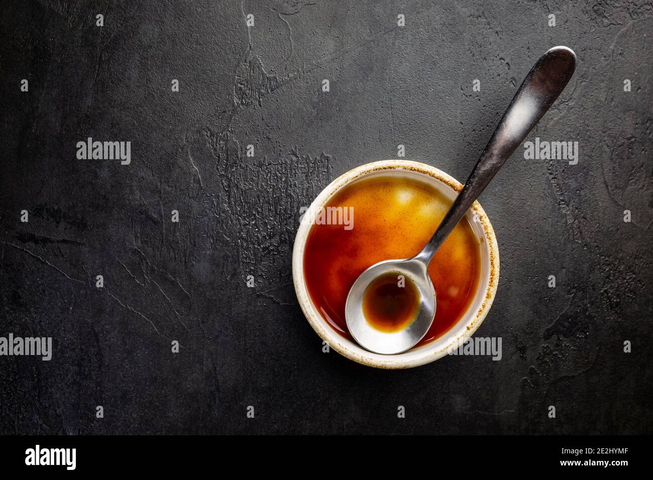 Worcestershire sauce in a bowl with spoon over black background, top view Stock Photo