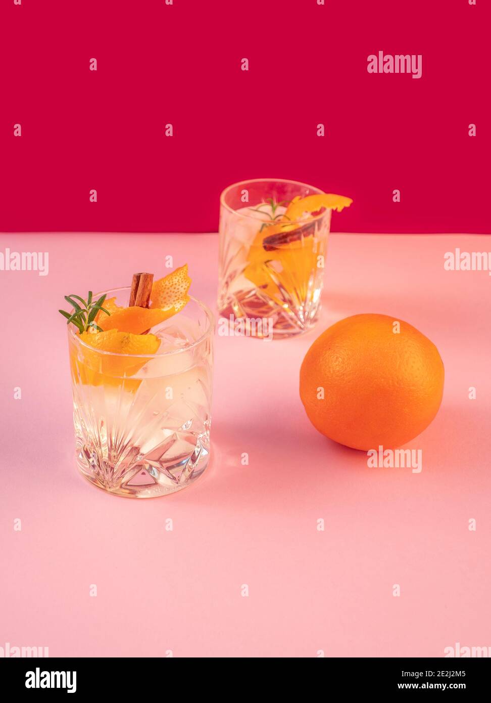 Two Gin and Tonic Drinks with Cinnamon and Tangerine isolated on pink coloured background Stock Photo