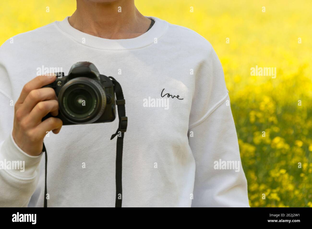 close up of a woman holding a camera, wearing a sweatshirt with 'love' written on it. Stock Photo