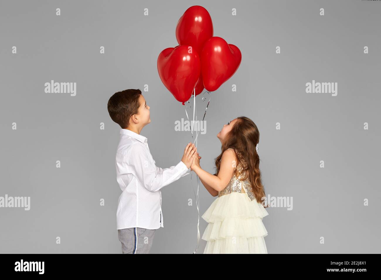 Happy couple of little girl and boy looking at red heart balloons ...