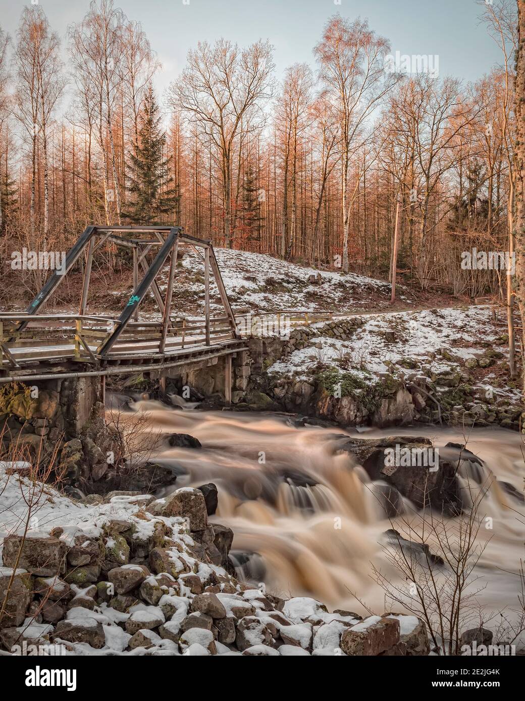 A closed rickety old bridge crosses a rapidly flowing waterfall at forsmollan near klippan . Stock Photo