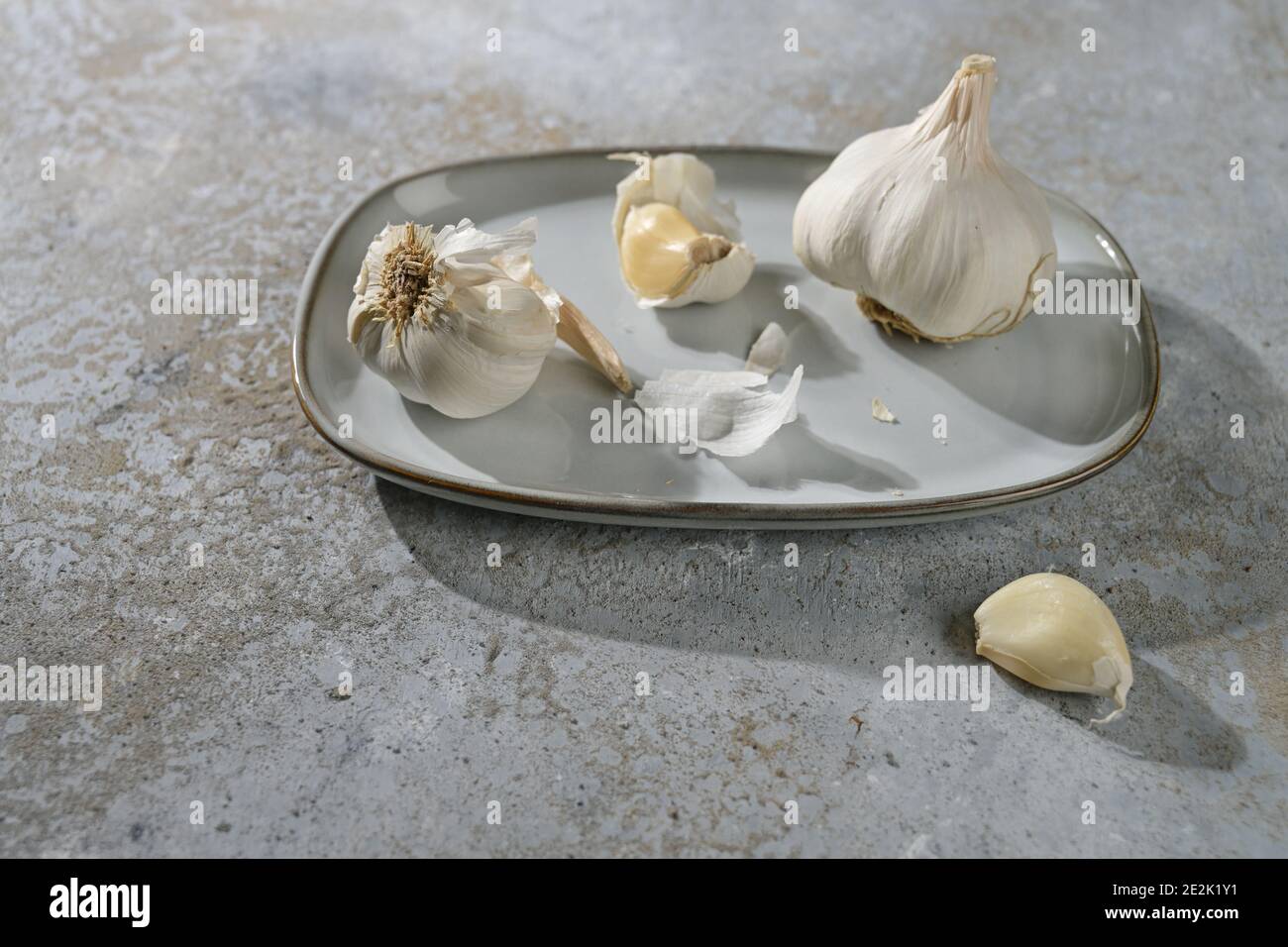 Garlic bulbs and cloves on a plate and a grey stone background, healthy food and medical plant for the cardiovascular system, copy space selected focu Stock Photo