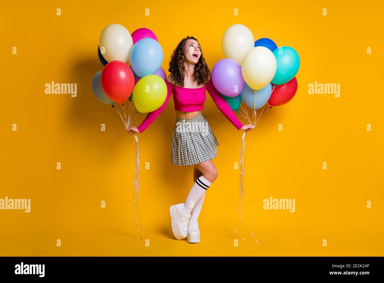 Full length body size photo of dreamy schoolgirl holding air balloons smiling wearing checkered skirt long socks cropped off-top isolated on bright Stock Photo