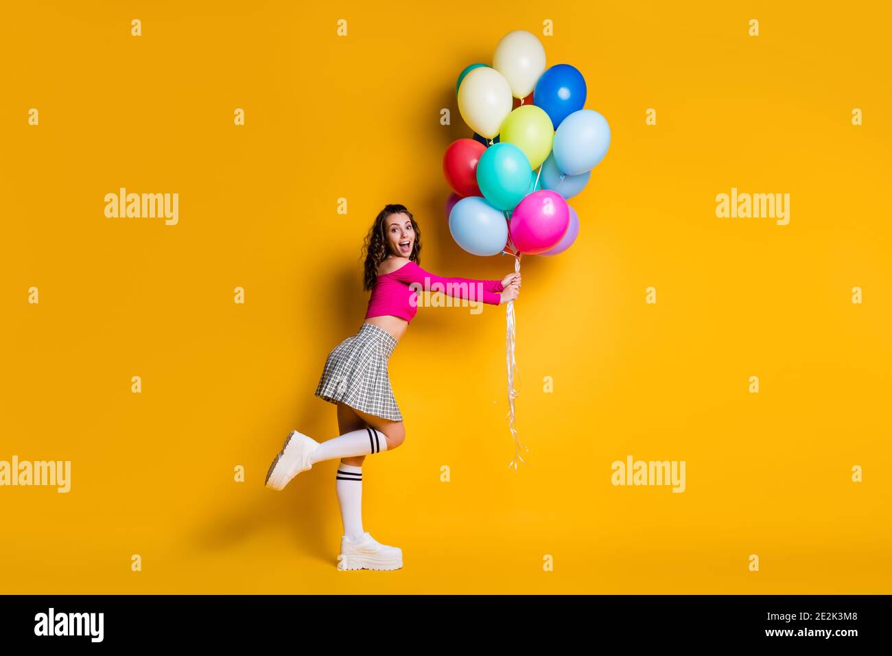 Full length body size photo of surprised impressed young girl holding air balloons smiling cheerful amazed isolated on bright yellow color background Stock Photo