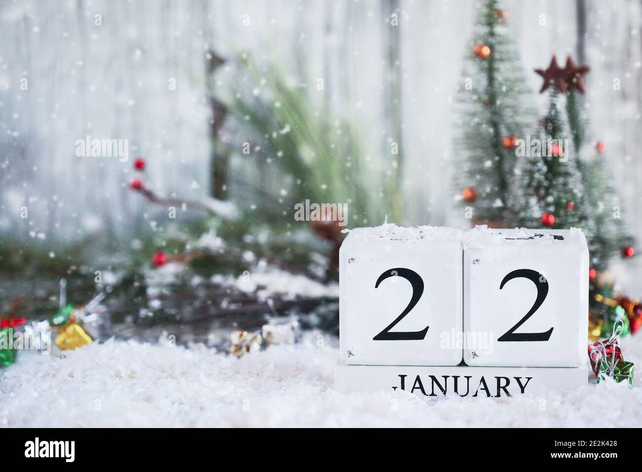 White wood calendar blocks with the date January 22nd and Christmas decorations with snow. Selective focus with blurred background. Stock Photo
