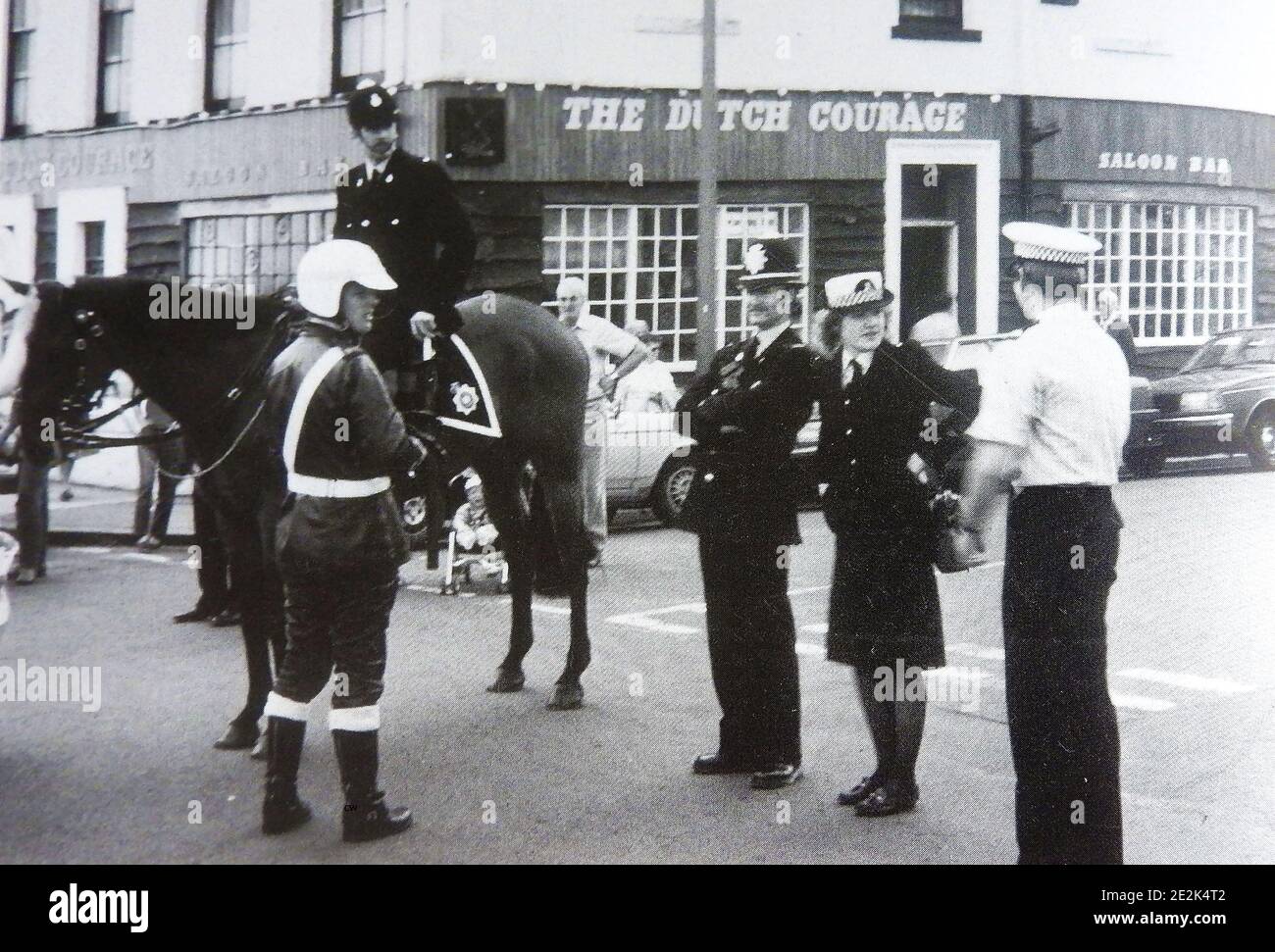 A circa late 1960's gathering of British police at Whitby, North Yorkshire's annual regatta, England showing the various uniforms and headgear worn by different branches of the service at that time. -- Mounted policeman on his horse , Motorcycle Cop, beat bobby (with helmet), Woman police officer and squad car driver (White shirt) Behind is the former Dutch Courage Bar (now defunct) which was part of the Royal Hotel on Whitby's West Cliff. Stock Photo