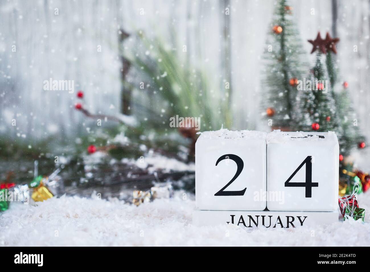 White wood calendar blocks with the date January 24th and Christmas decorations with snow. Selective focus with blurred background. Stock Photo
